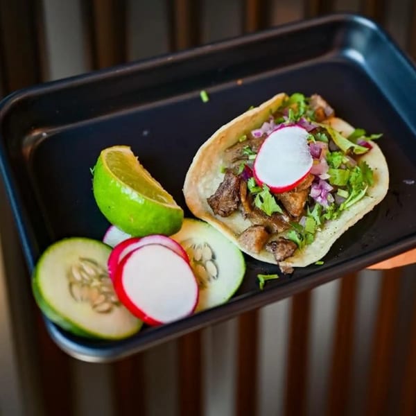 A Tacos Number Juan taco with meat, cilantro, onions, radish, lime, and cucumber on a black tray.