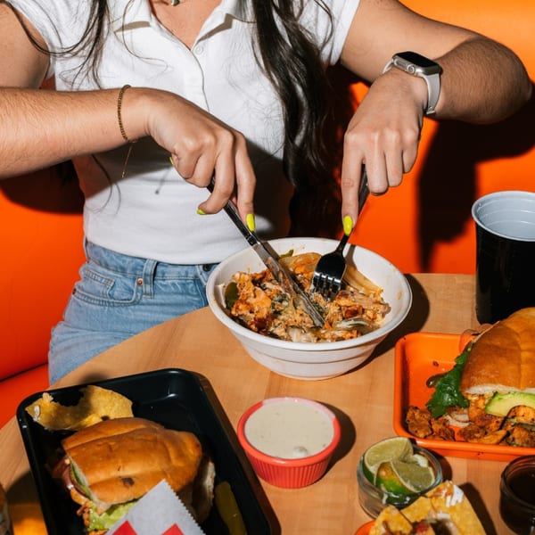 A person in a white shirt and jeans eats a bowl of Tacos Number Juan's Mexican food.