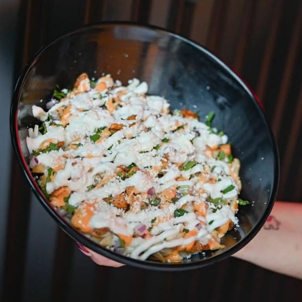 A black bowl filled with Tacos Number Juan's Mexican street fries, topped with sauces, cheese, and cilantro.