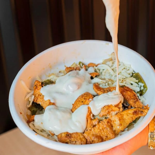 Creamy white sauce being poured over a bowl of chicken, rice, and vegetables.