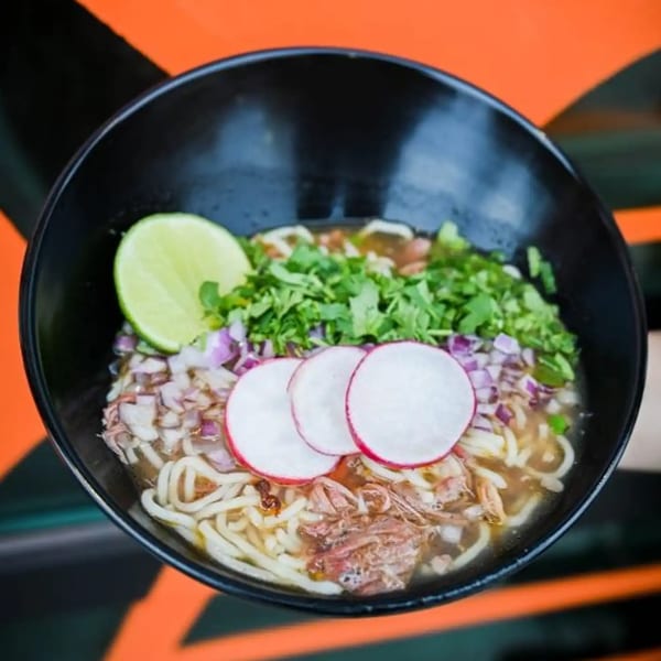 A black bowl of Tacos Number Juan's Mexican ramen with noodles, meat, cilantro, radishes, and lime.