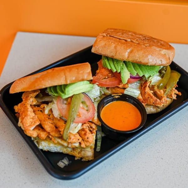 Two Mexican tortas with chicken, avocado, lettuce, tomato, and pickled peppers, served with orange sauce.